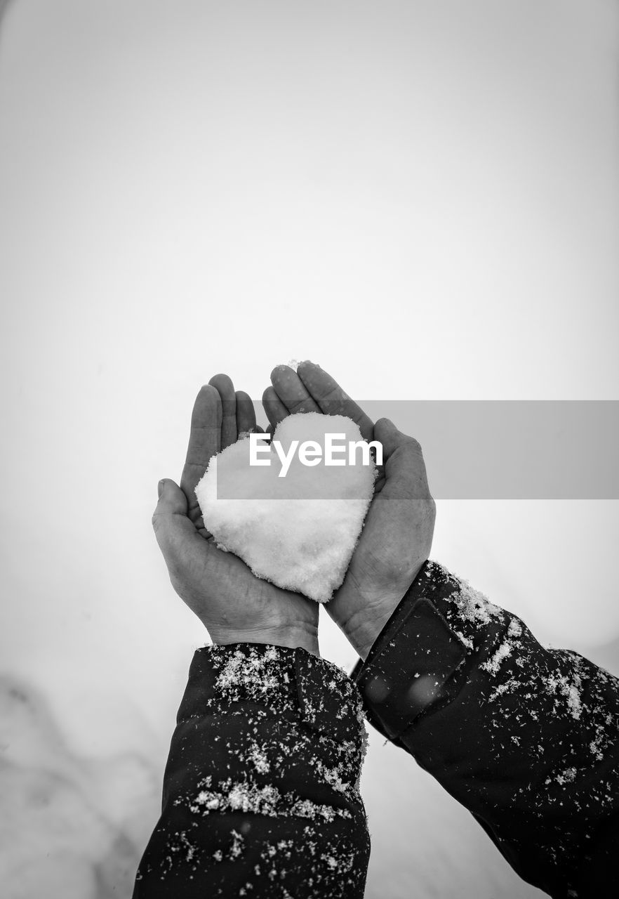 Cropped hand of woman holding heart shape snow in hand outdoors