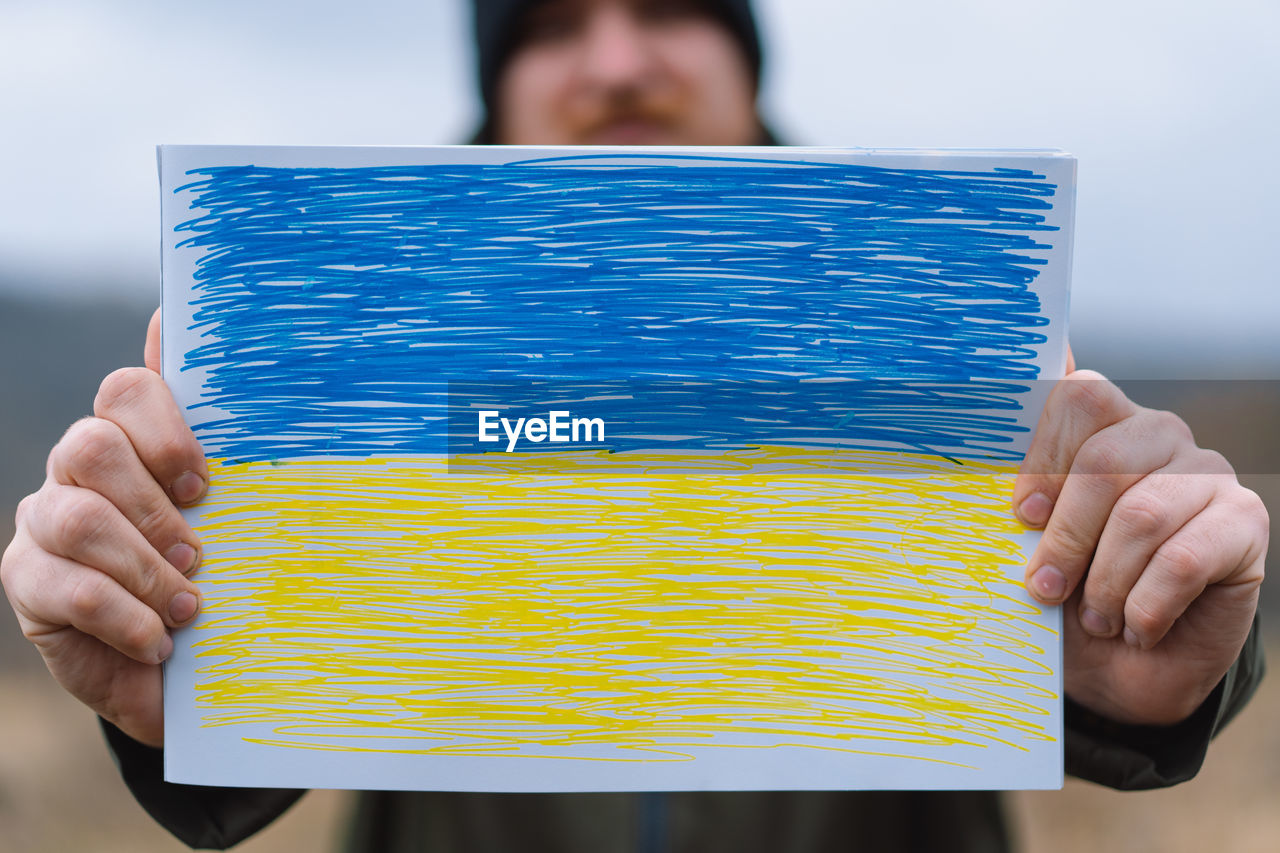 Cropped hands of woman holding multi colored pencils against sky