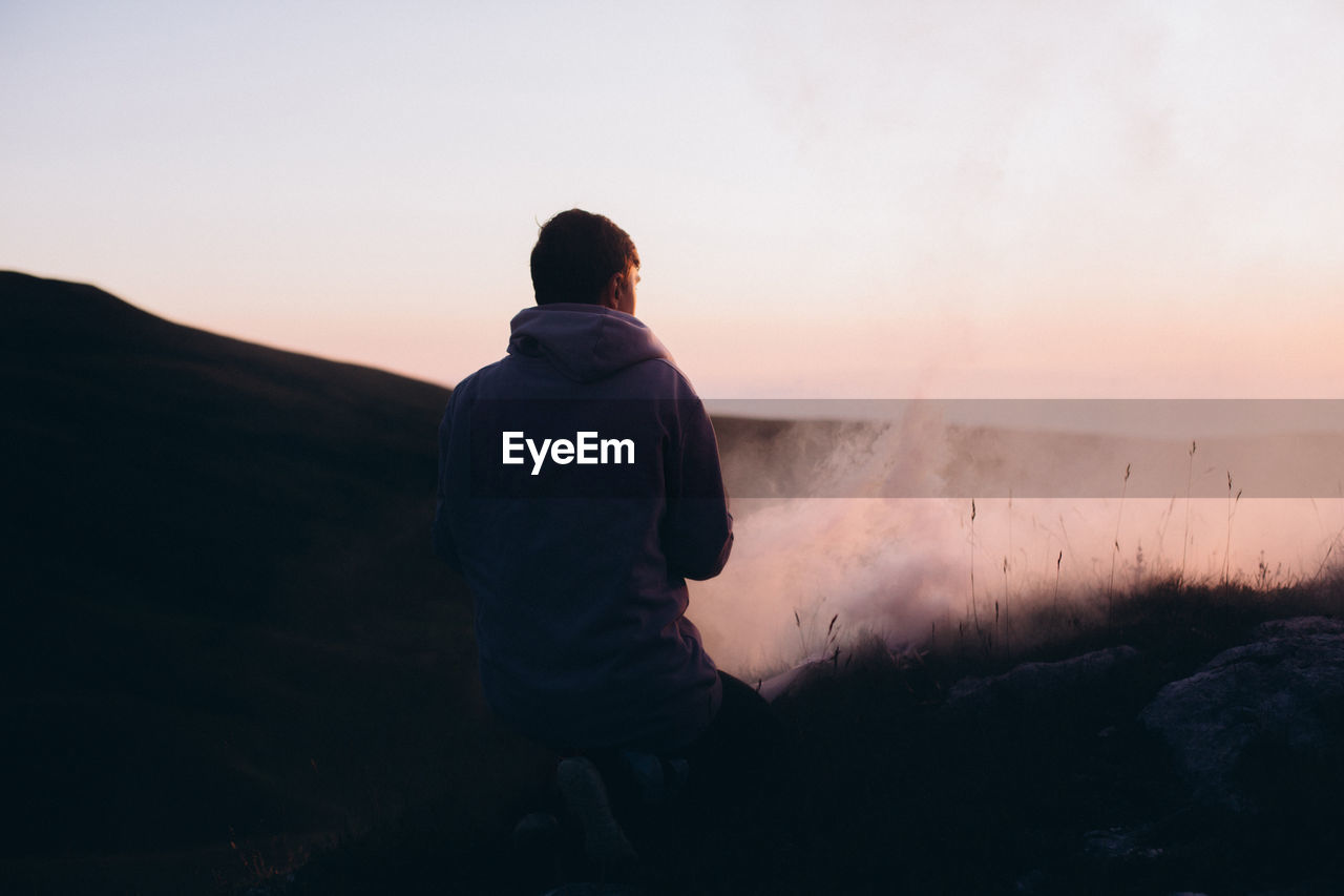 Rear view of man kneeling on mountain during sunset