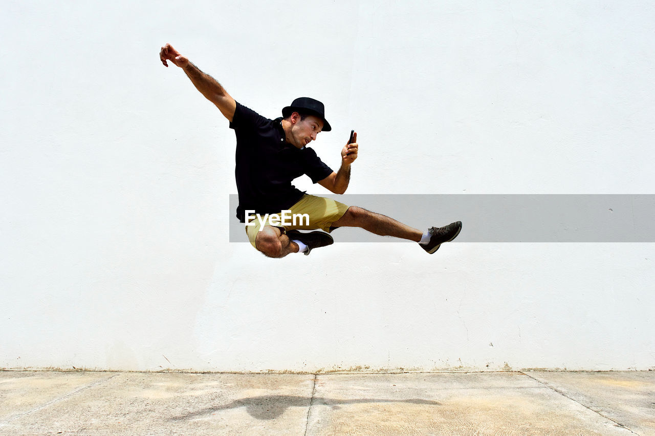 Man using smart phone while jumping against wall