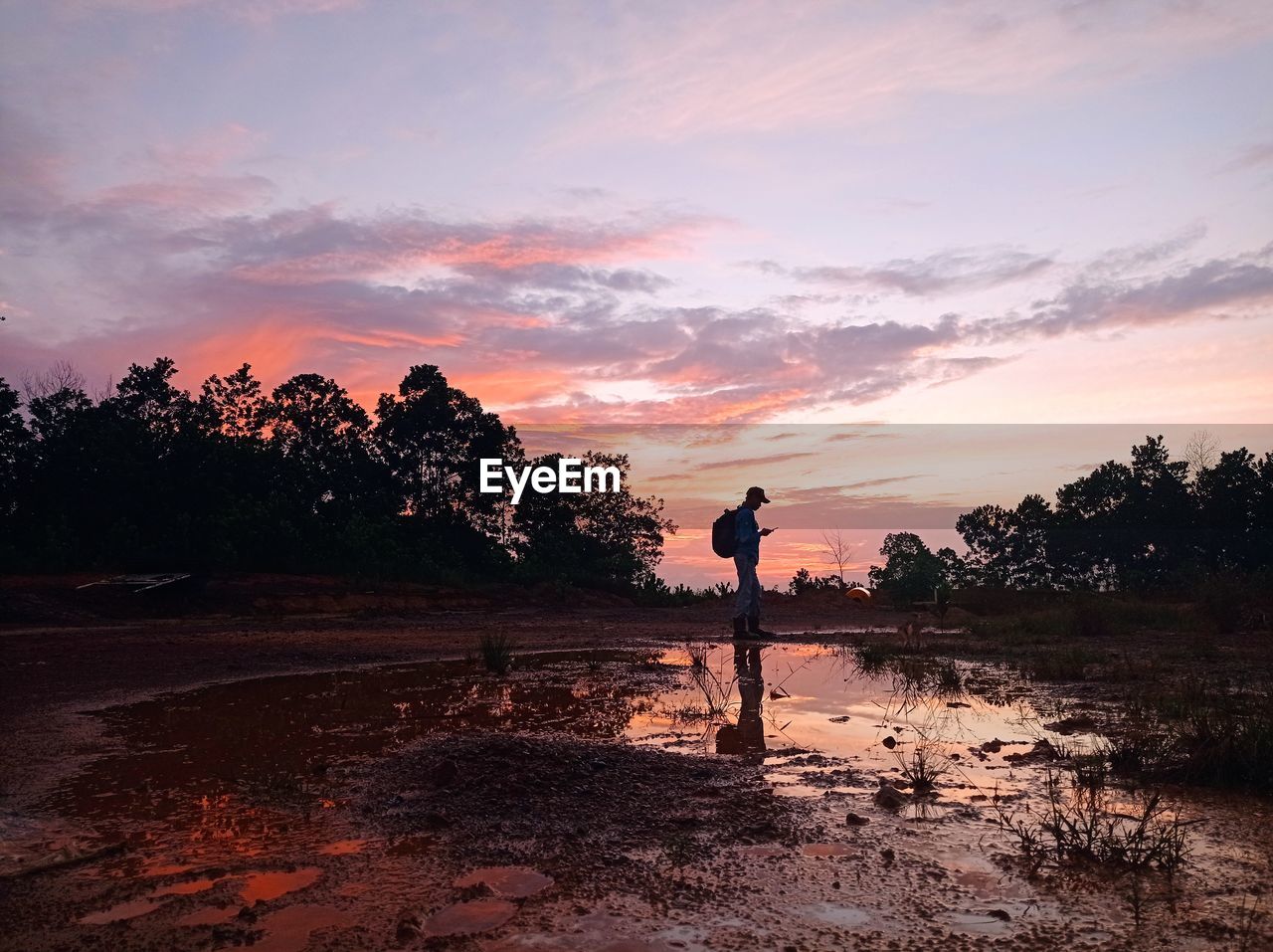 sky, sunset, dawn, evening, horizon, one person, nature, water, tree, cloud, silhouette, land, men, environment, landscape, beauty in nature, full length, adult, plant, sunlight, reflection, lifestyles, leisure activity, scenics - nature, beach, sea, tranquility, activity, outdoors, shore, orange color, standing, occupation, sports, sun
