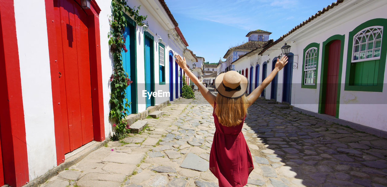 Beautiful young woman with raised arms walking in colorful historic town of paraty