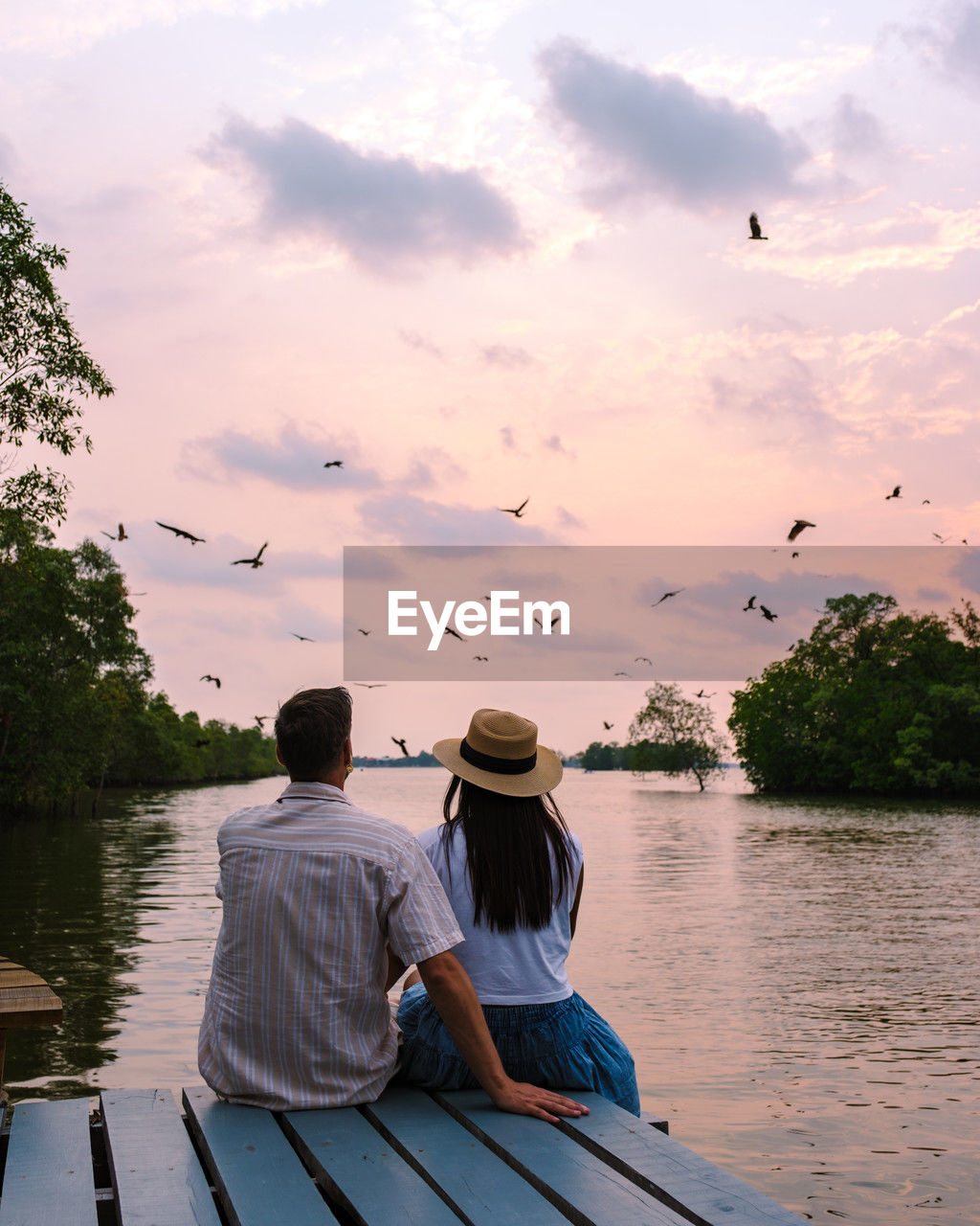 rear view of man sitting on boat on lake against sky during sunset