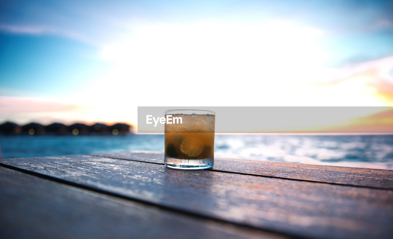 Close-up of glass of whisky on table against sky