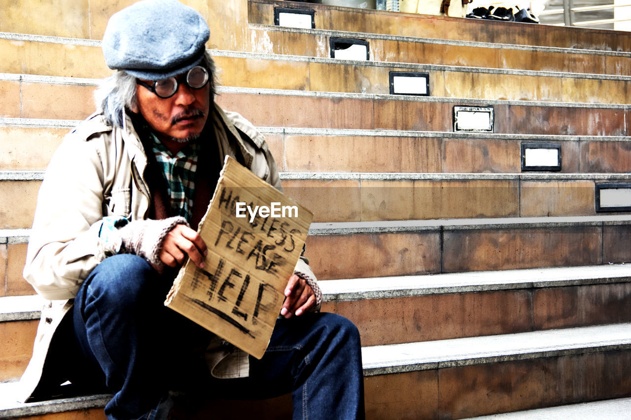 Beggar holding placard while sitting on steps