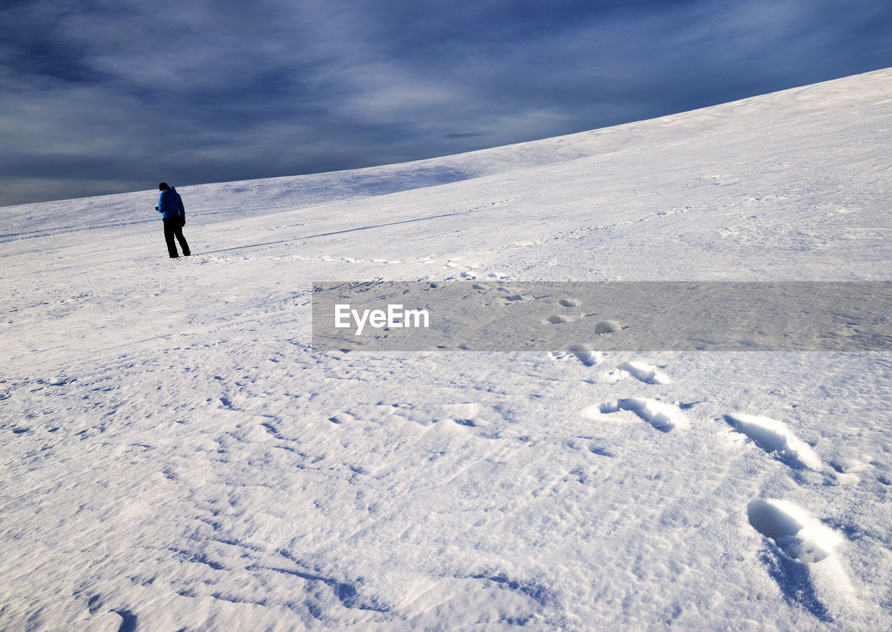 Rear view of hiker standing on snow covered mountain against sky