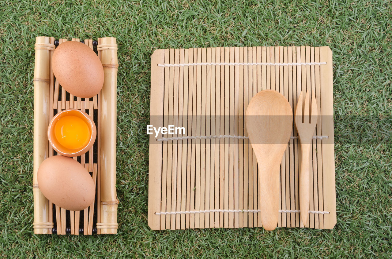Directly above shot of egg in spoon on bamboo mat over grass