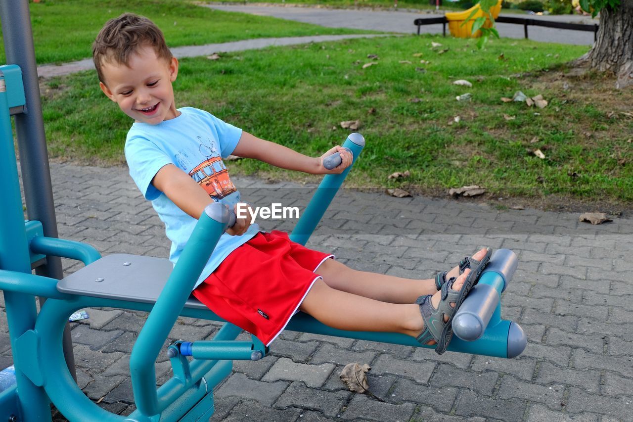 Full length of happy boy enjoying on play equipment at park