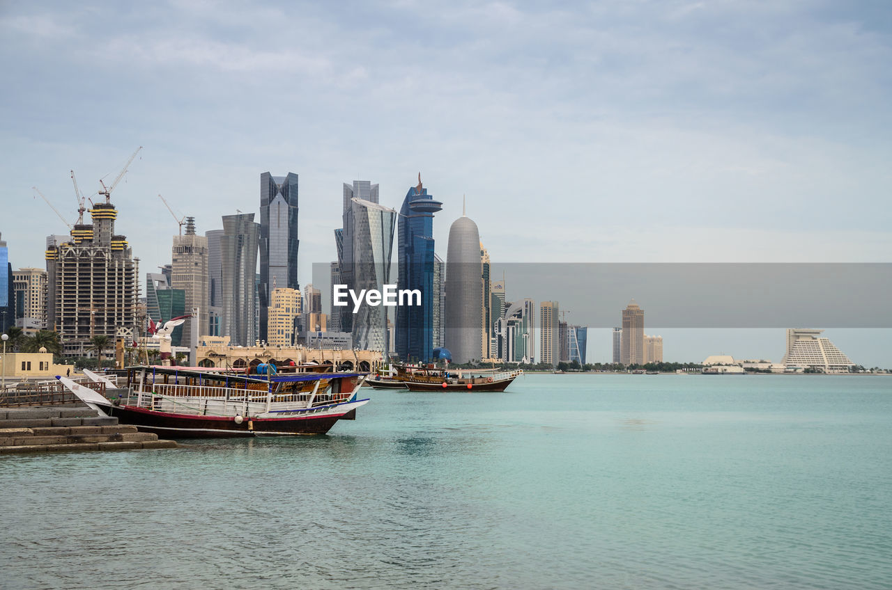 Sea by modern buildings in city against sky