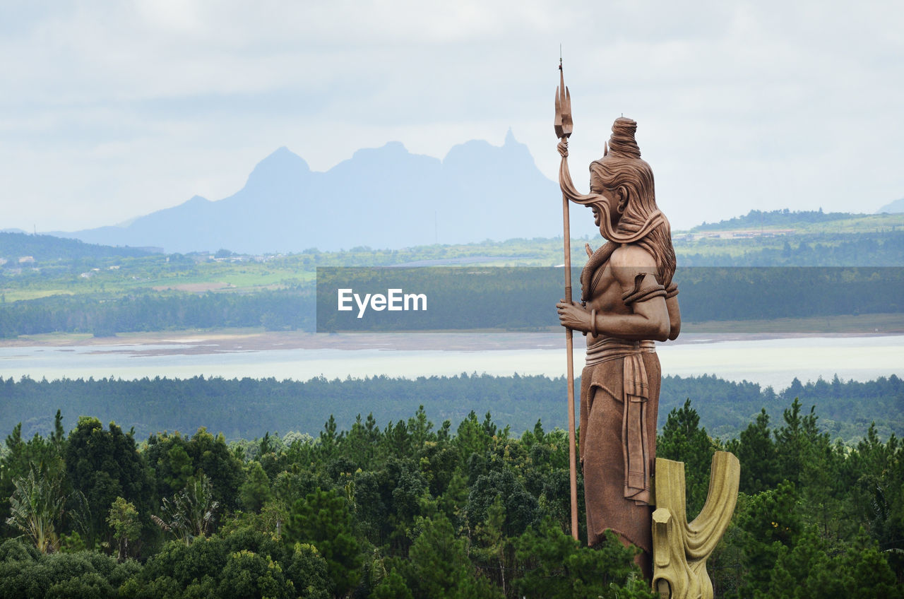 Shiva statue by trees against river