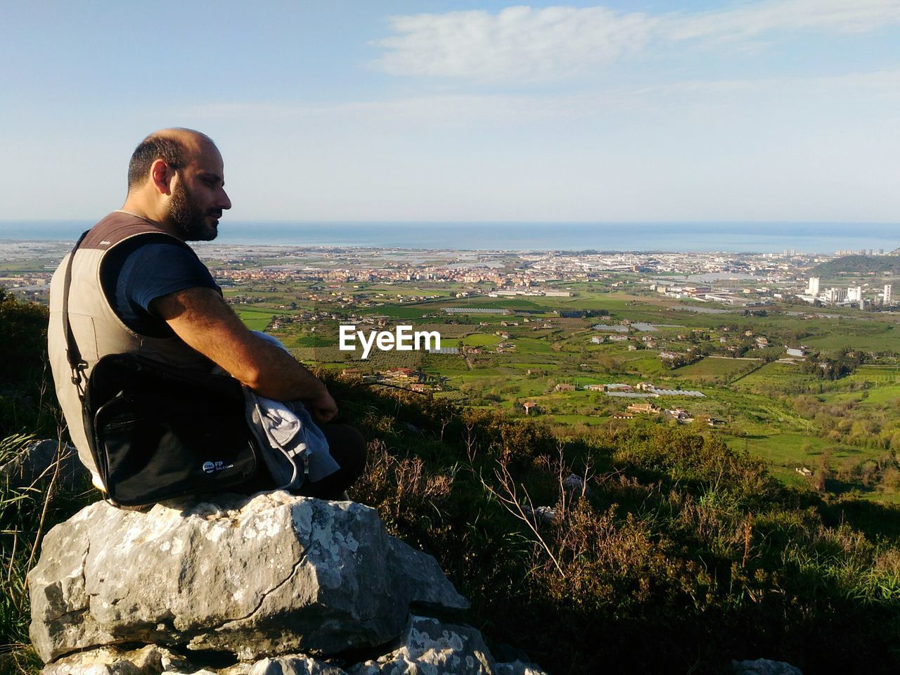 Man looking at view while sitting on rock against sky