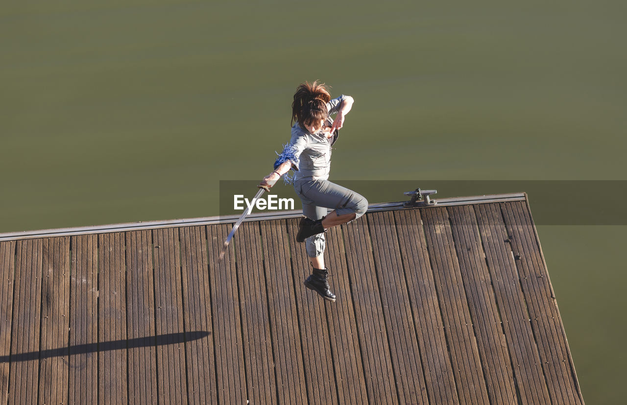 Female athlete performing martial arts stunt with sword while jumping on promenade during sunny day