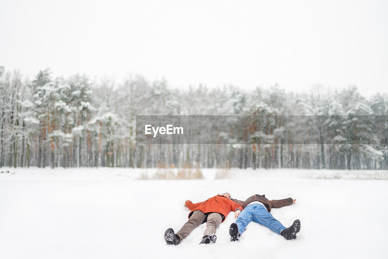 Full length of loving couple lying having fun on snow covered forest