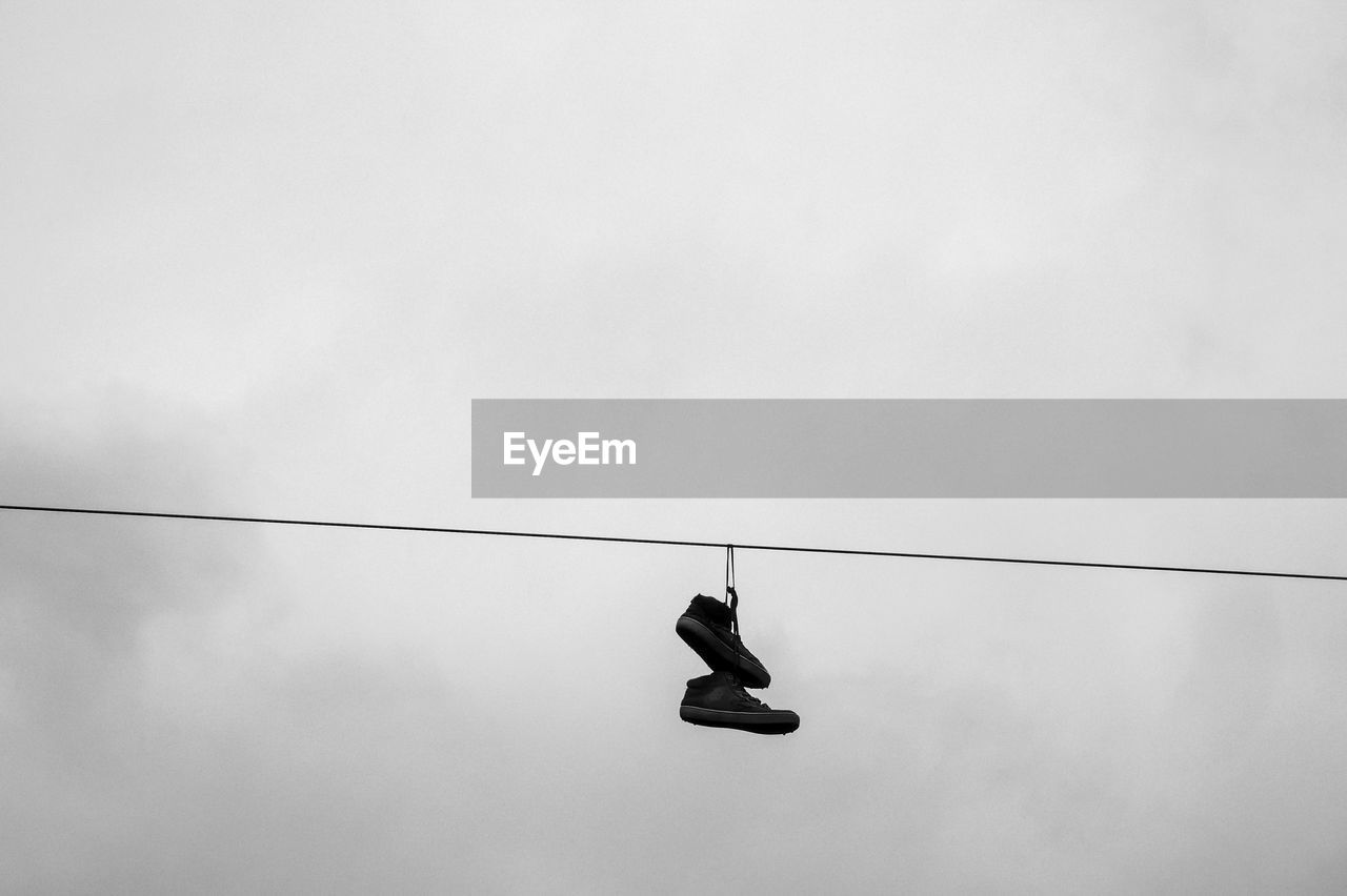 LOW ANGLE VIEW OF SHOES HANGING ON CABLE