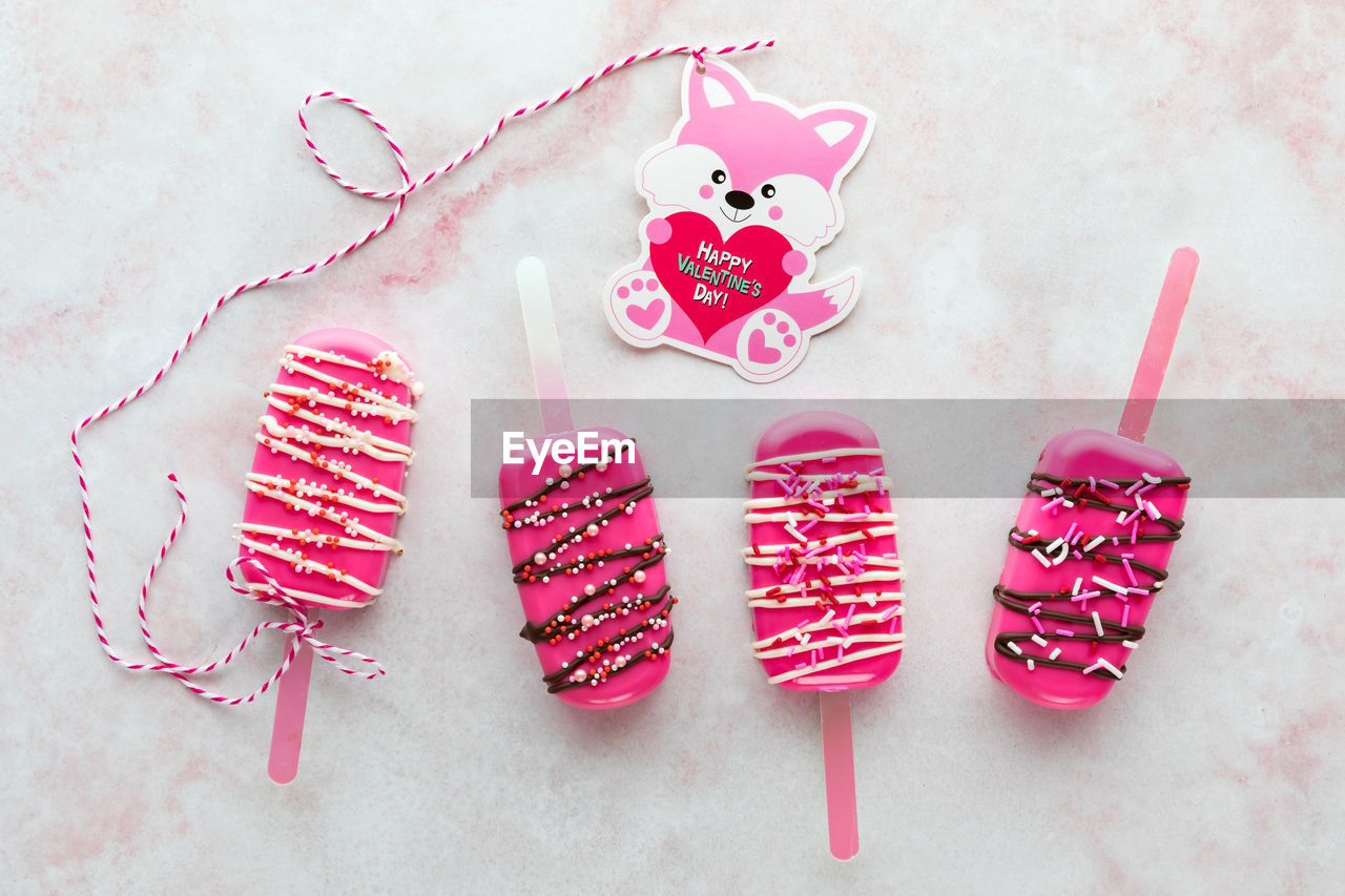 Homemade decorated valentine cakesicles with a valentine card attached to one.