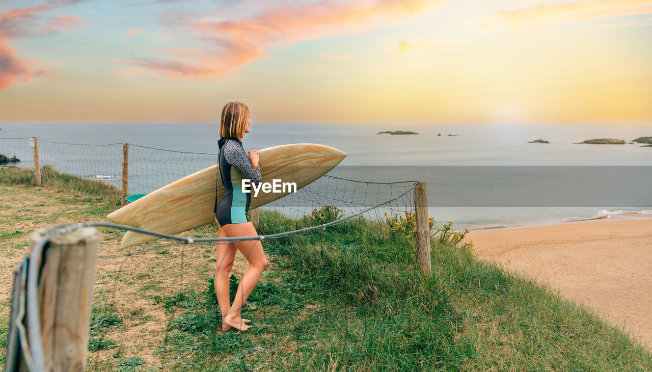 Surfer woman with surfing suit and surfboard looking at the beach