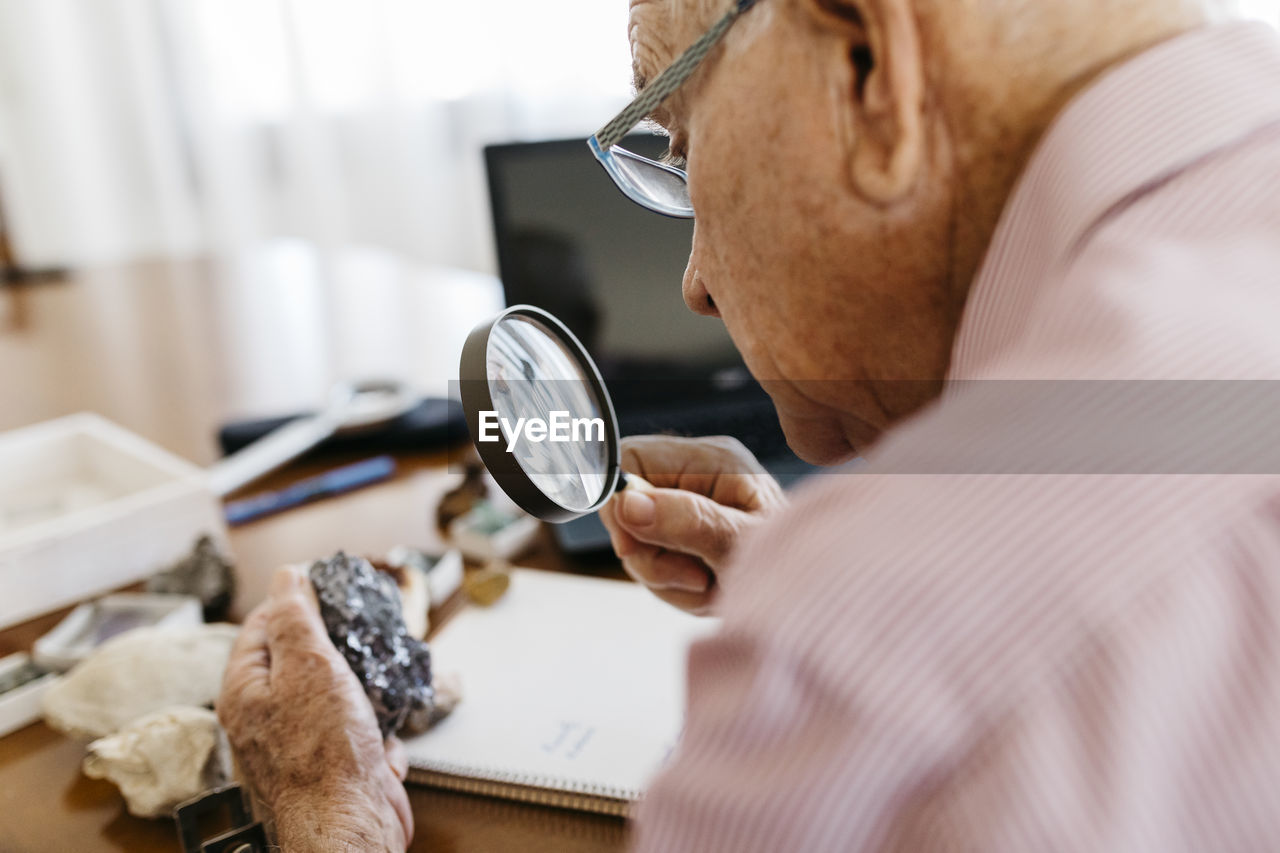 Retired senior male looking through magnifying glass at mineral