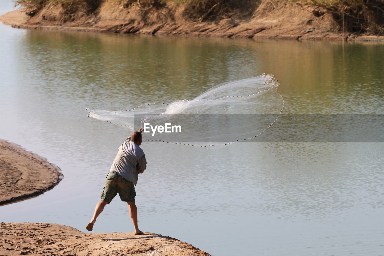 Rear view of man casting a fish net in a creek