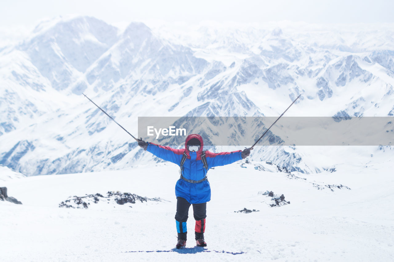 Man with ski poles standing on snow against snowcapped mountains