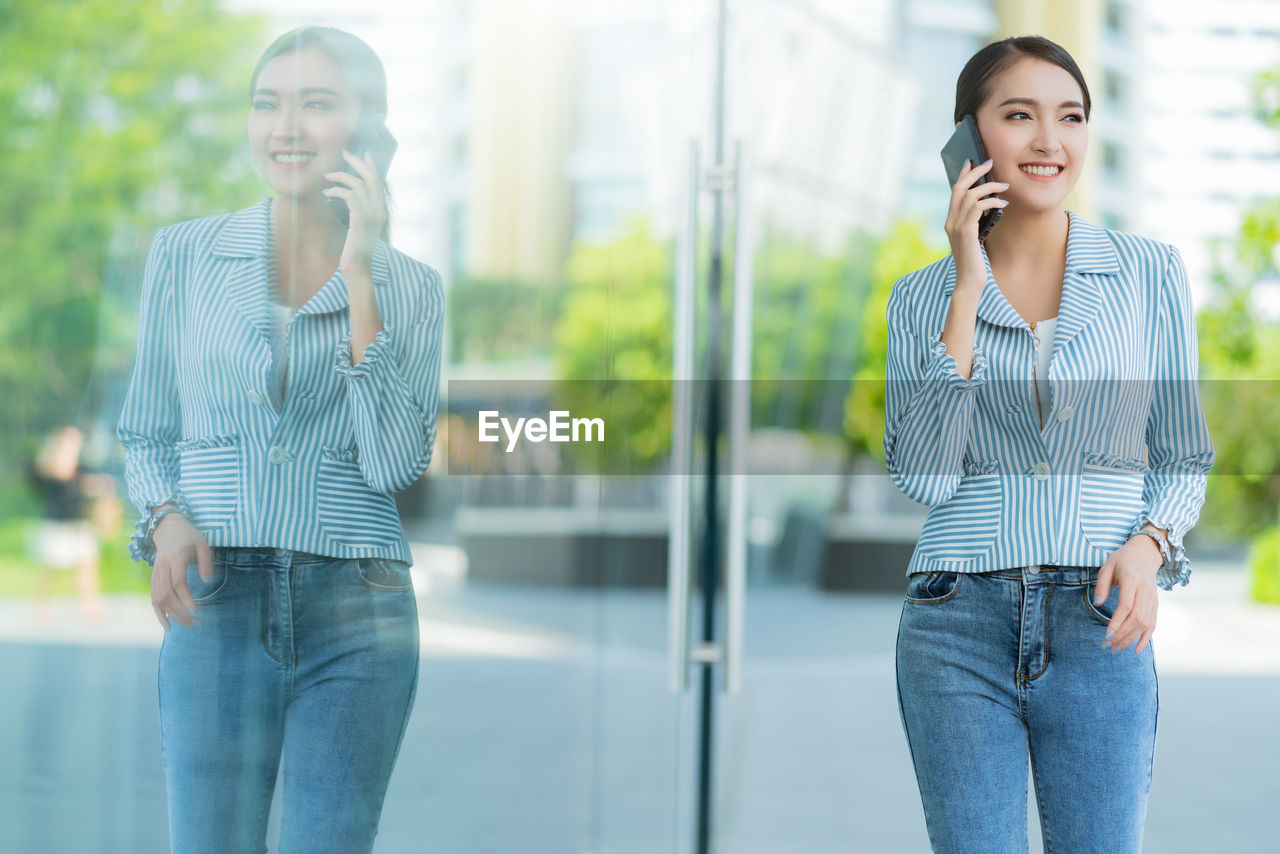 YOUNG WOMAN USING MOBILE PHONE WHILE STANDING ON CAMERA AT HOME