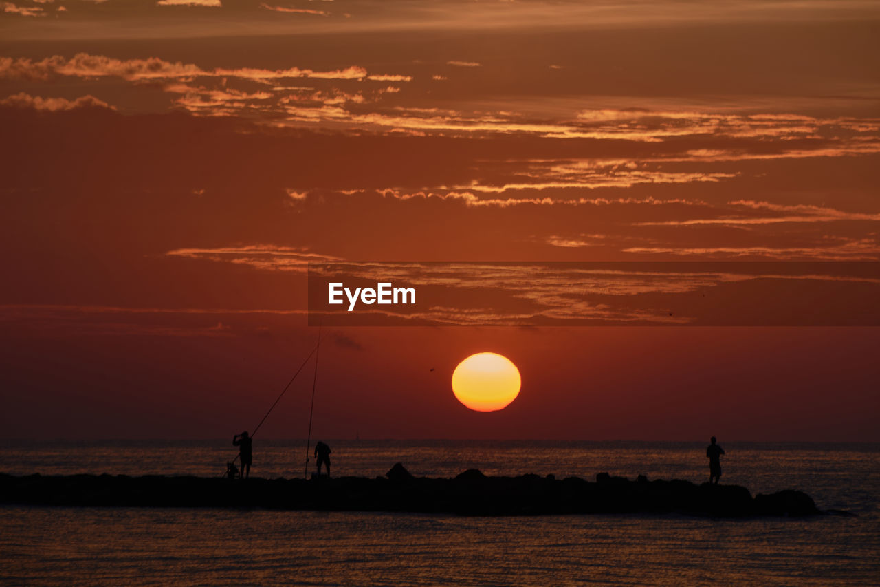 The sun appears among the fishermen on the breakwater