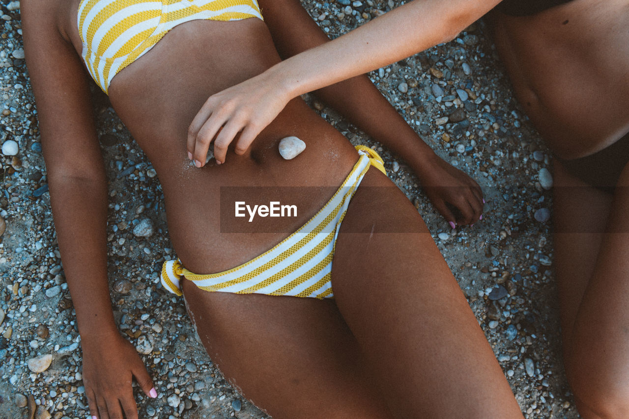 Midsection of women wearing bikini lying at beach