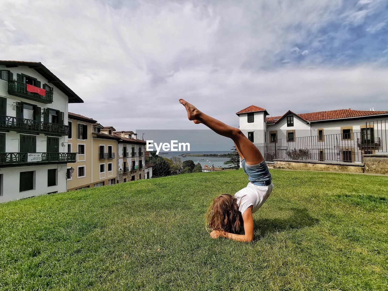 Full length of girl doing handstand on grass against sky