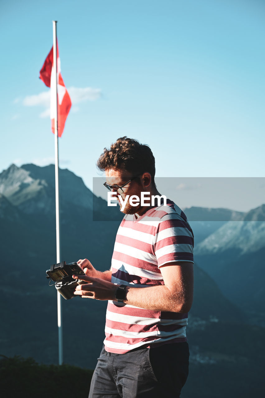 Young man using drone remote control against sky and mountains 