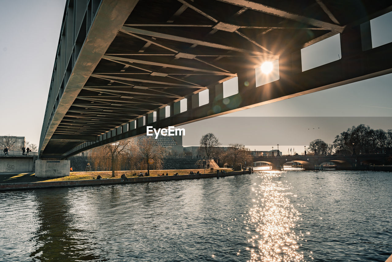 Bridge over river by illuminated buildings against sky in city