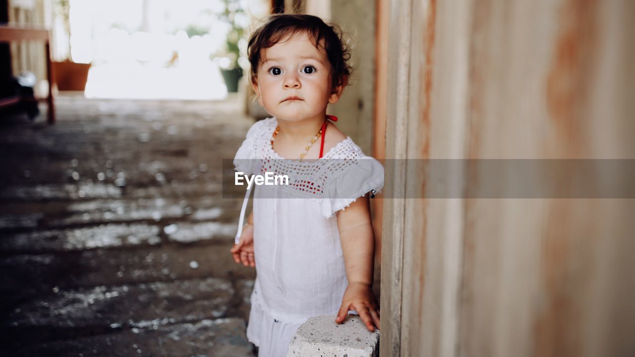 PORTRAIT OF CUTE GIRL LOOKING AWAY WHILE STANDING AGAINST WALL