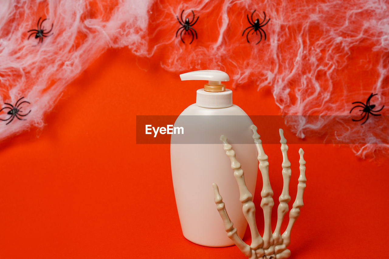 Cosmetic bottle with oil or soap on red halloween background with spiders and skeleton hands