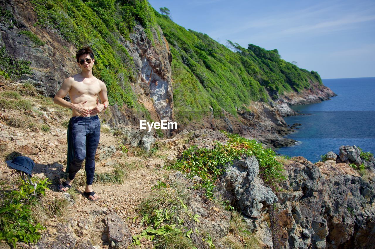 Man standing on rock by sea against sky with peninsular ending 