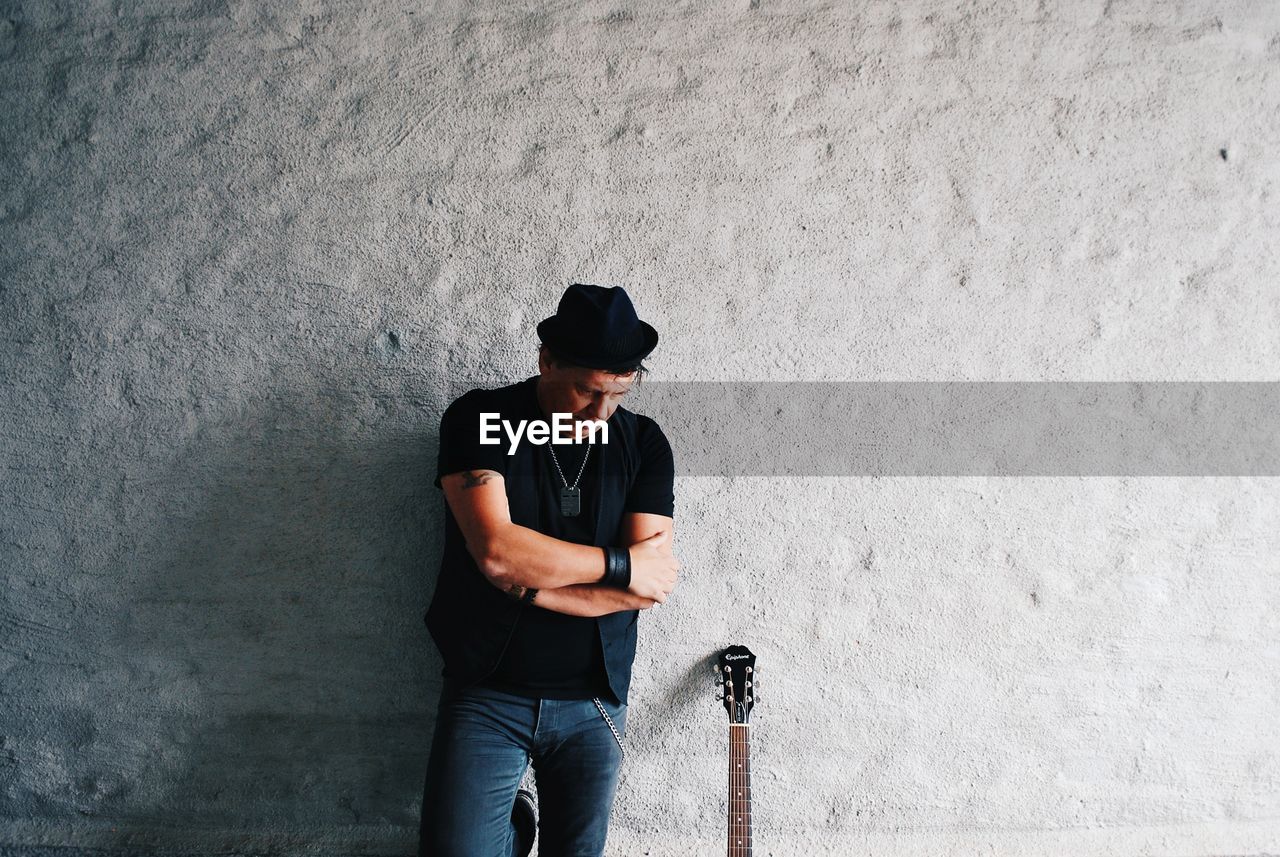 FULL LENGTH OF YOUNG MAN LOOKING THROUGH CAMERA AGAINST WALL