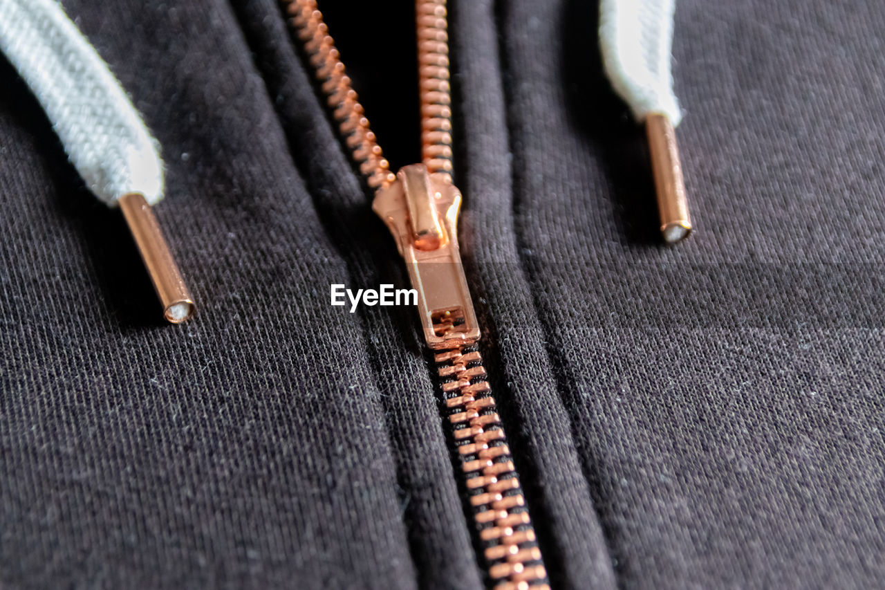 Copper colored fashion zipper in close-up macro view showing black sweatshirt with opened zipper