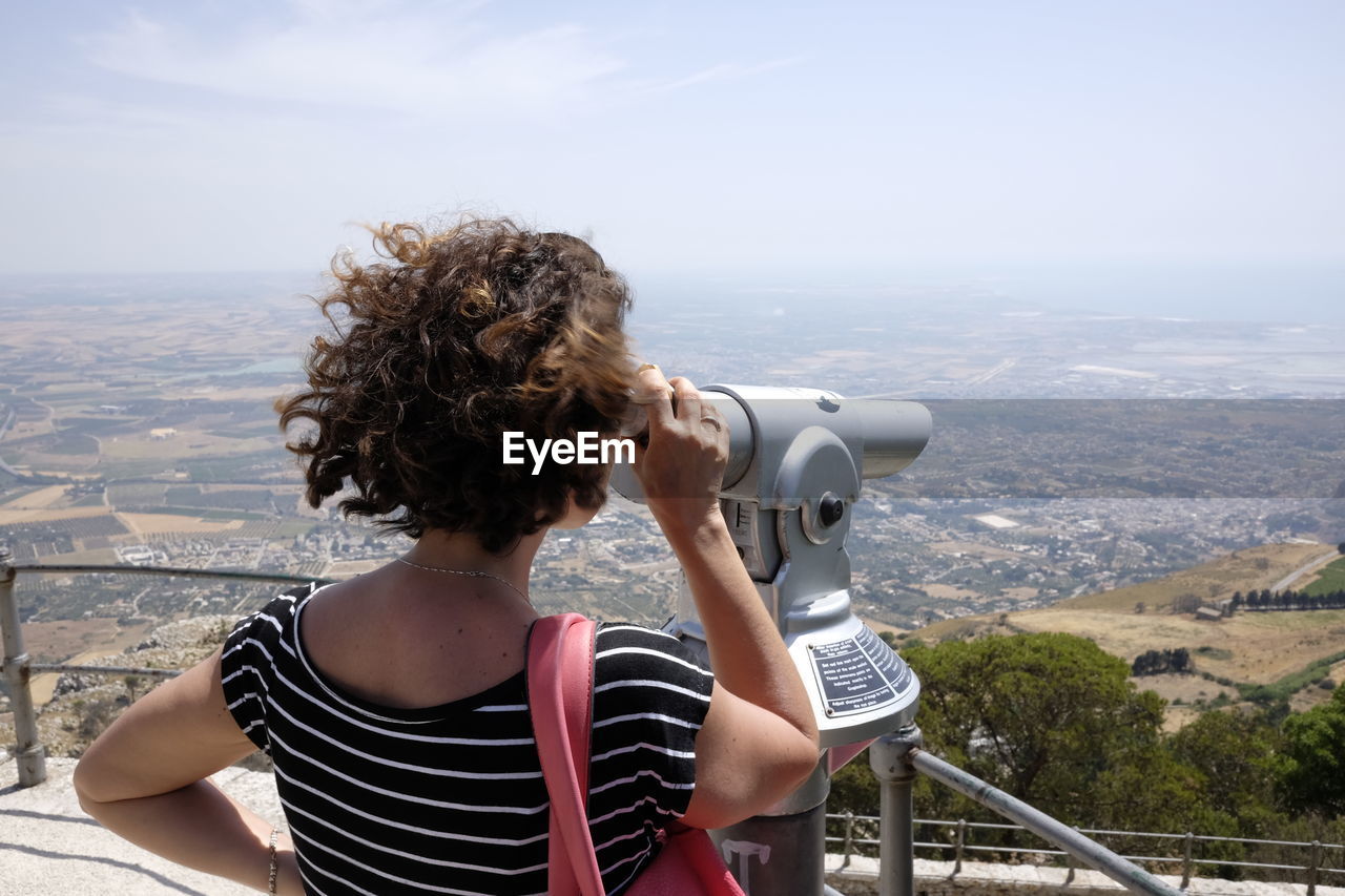 Rear view of woman looking through coin-operated binoculars from observation point at erice