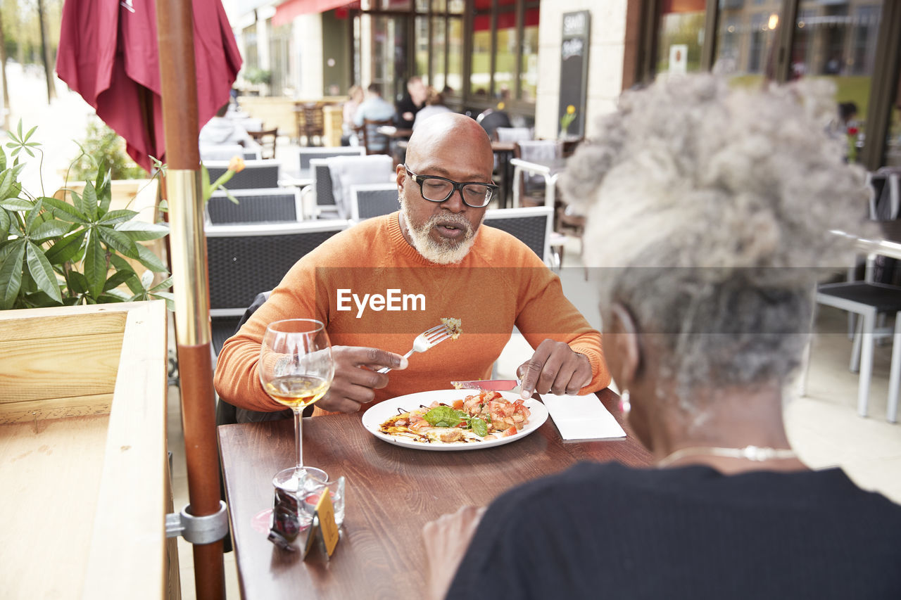 Bald man eating food with woman at sidewalk cafe