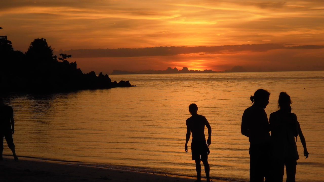 Silhouette people standing at beach during sunset