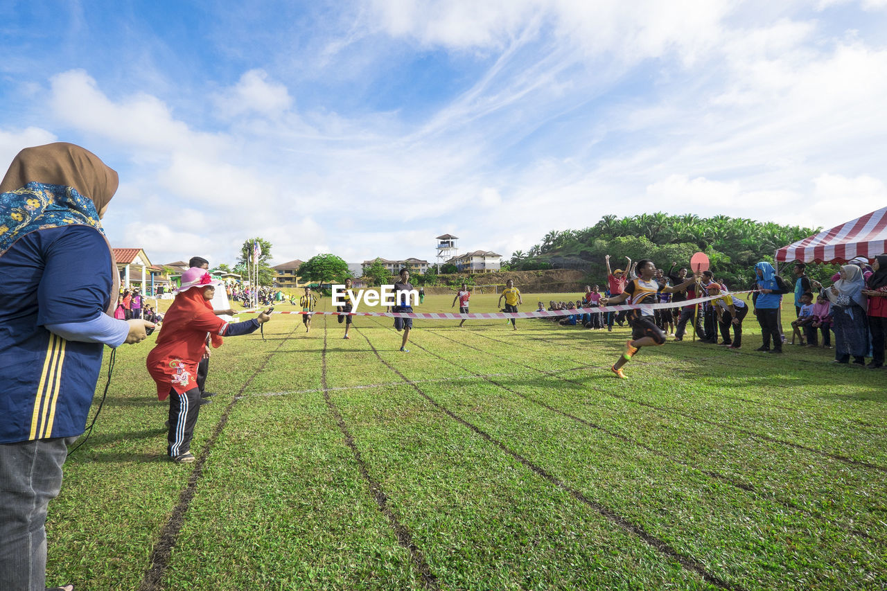 GROUP OF PEOPLE PLAYING SOCCER ON LANDSCAPE AGAINST SKY