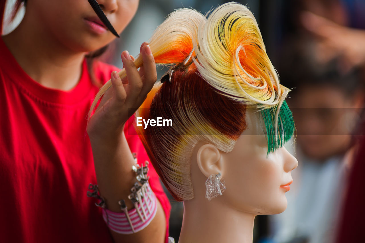 Young woman combing wig of mannequin