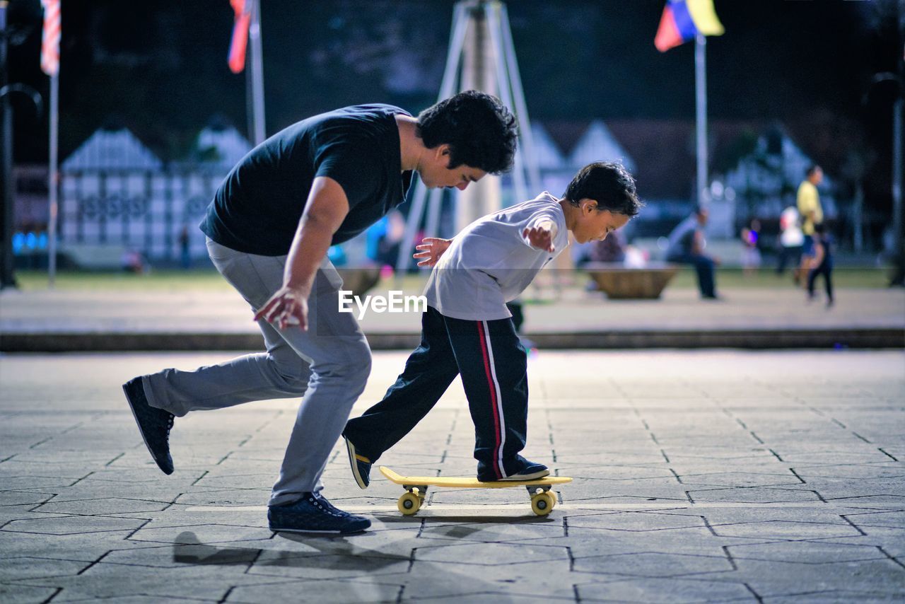 Side view of coach teaching student balancing on skateboard at park