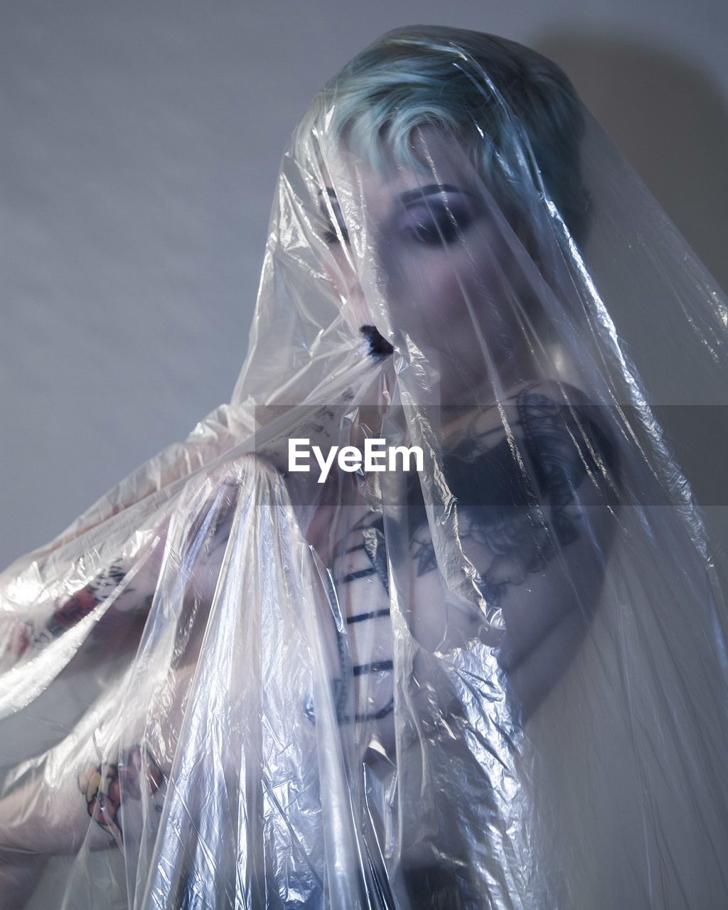 Young woman covered with plastic bag while standing against wall