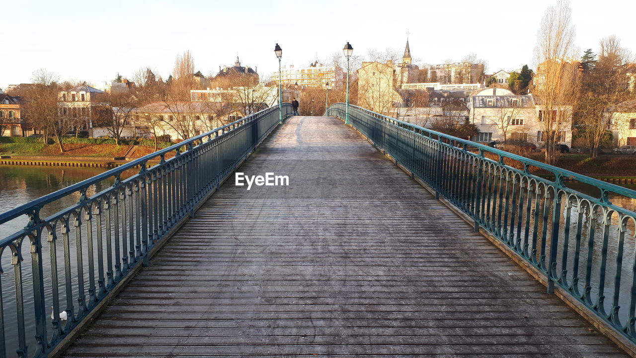 FOOTBRIDGE OVER RIVER AMIDST BUILDINGS AGAINST SKY
