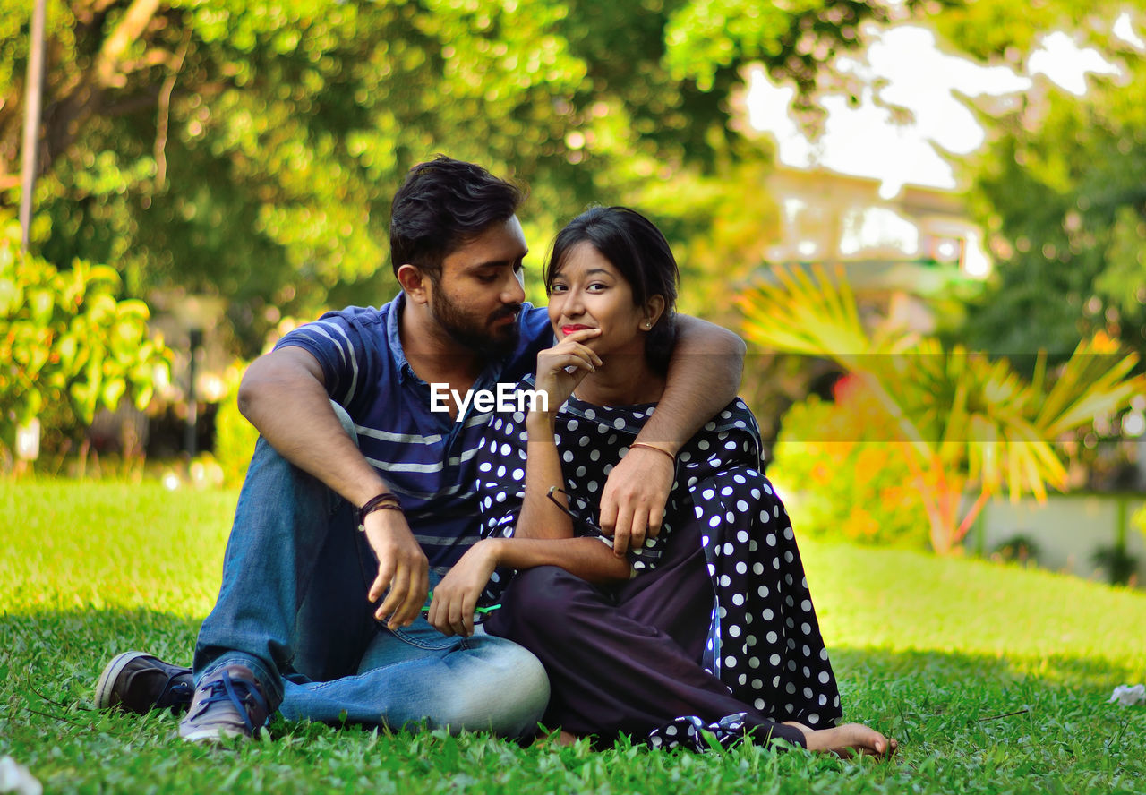 Portrait of young woman sitting with boyfriend at park