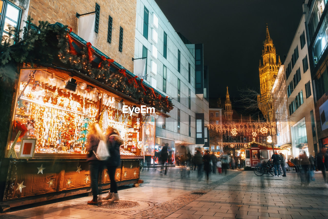 People on illuminated street amidst during christmas in city at night