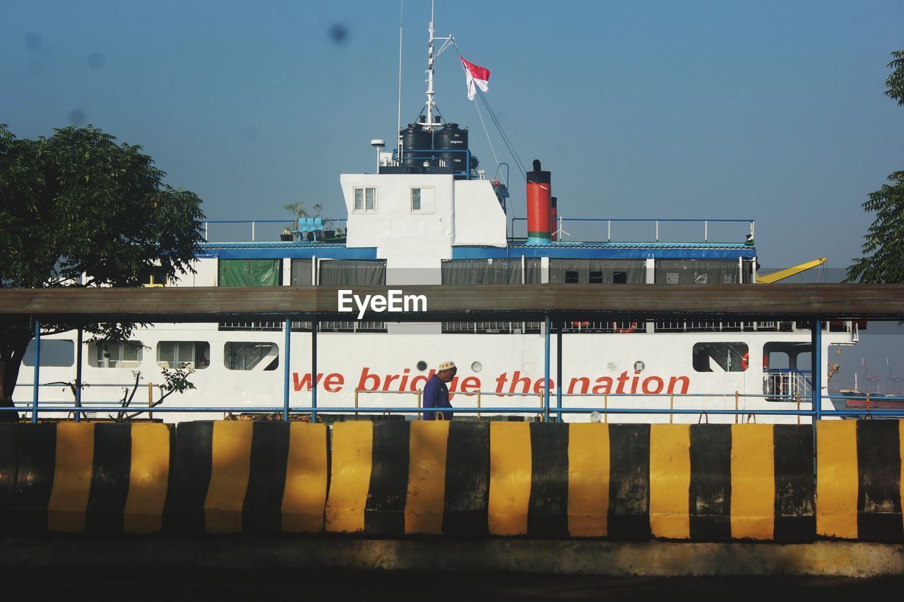 ferry, vehicle, transportation, ship, transport, mode of transportation, architecture, cargo ship, watercraft, water, nature, freight transport, nautical vessel, tugboat, sky, text, flag, boat, built structure, passenger ship, no people, outdoors, western script, communication, security, day, tree, building exterior, channel, government