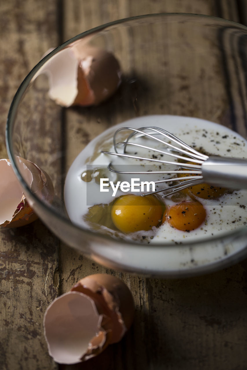 High angle view of wire whisk and eggs in bowl on table