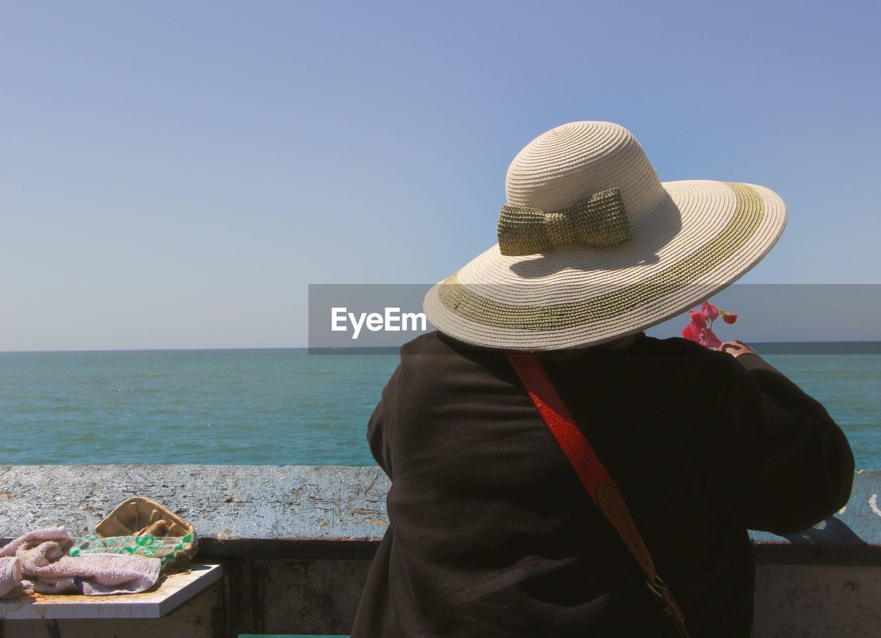 Rear view of woman wearing hat against sea at beach