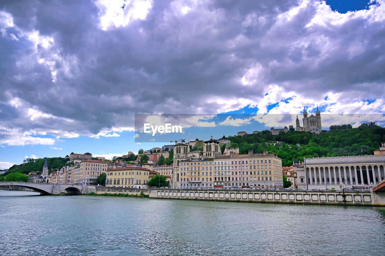 BUILDINGS BY RIVER AGAINST SKY IN CITY