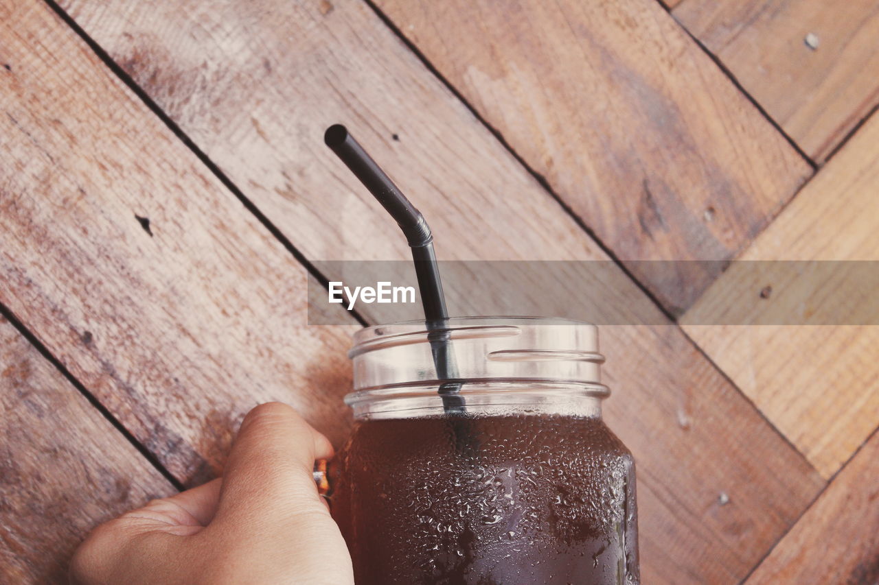 Cropped hand having drink in jar by wooden wall