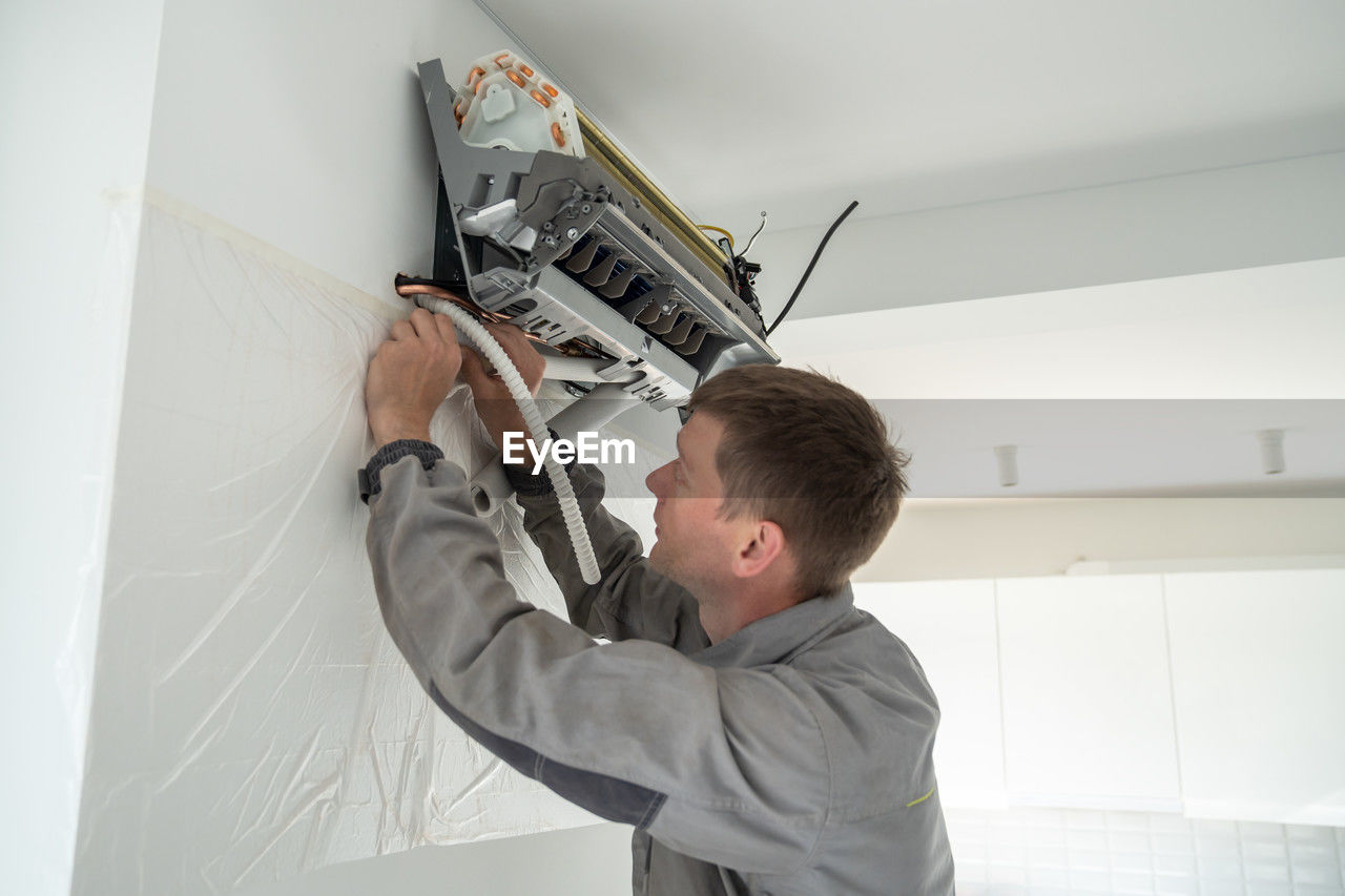 Installing air conditioner in house. man specialist wearing work uniform fixing air cooler system.